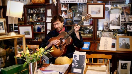 A musician holding a guitar inside Sweny's Pharmacy in Dublin City