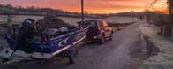 A jeep along the side of a road with a boat on a trailer at a colourful sunset