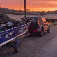 A jeep along the side of a road with a boat on a trailer at a colourful sunset