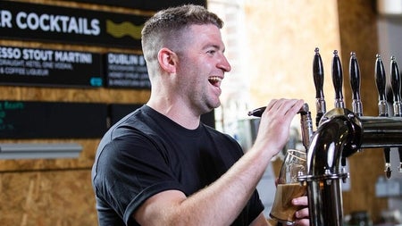A laughing barman pours a pint of Guinness