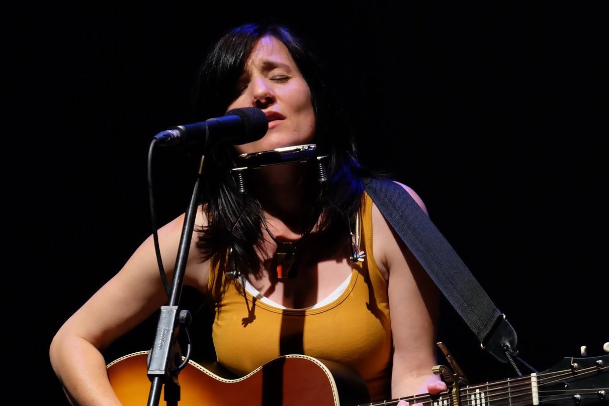 A woman is singing into a mic playing a guitar