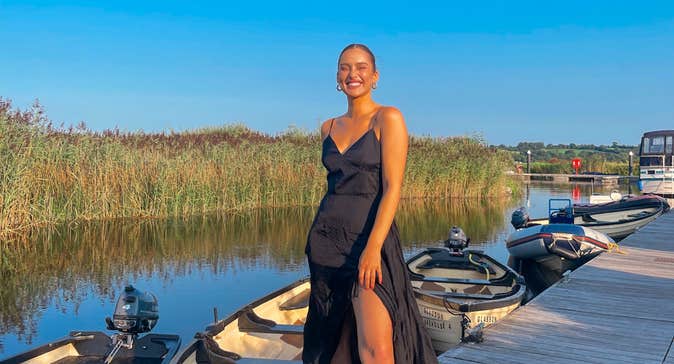 Roz Purcell wearing a black dress standing on a deck in front of a row of boats at Glasson Lakehouse, Westmeath