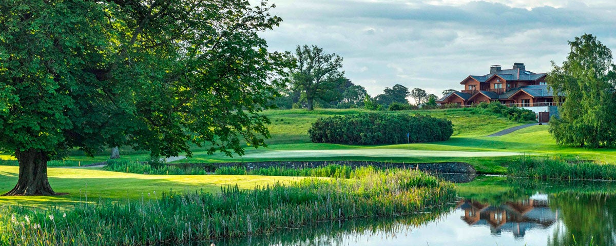 A view from the golf course through greenery and over water of the club house