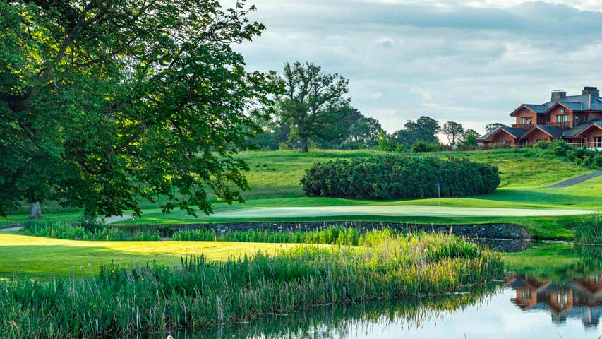 A view from the golf course through greenery and over water of the club house