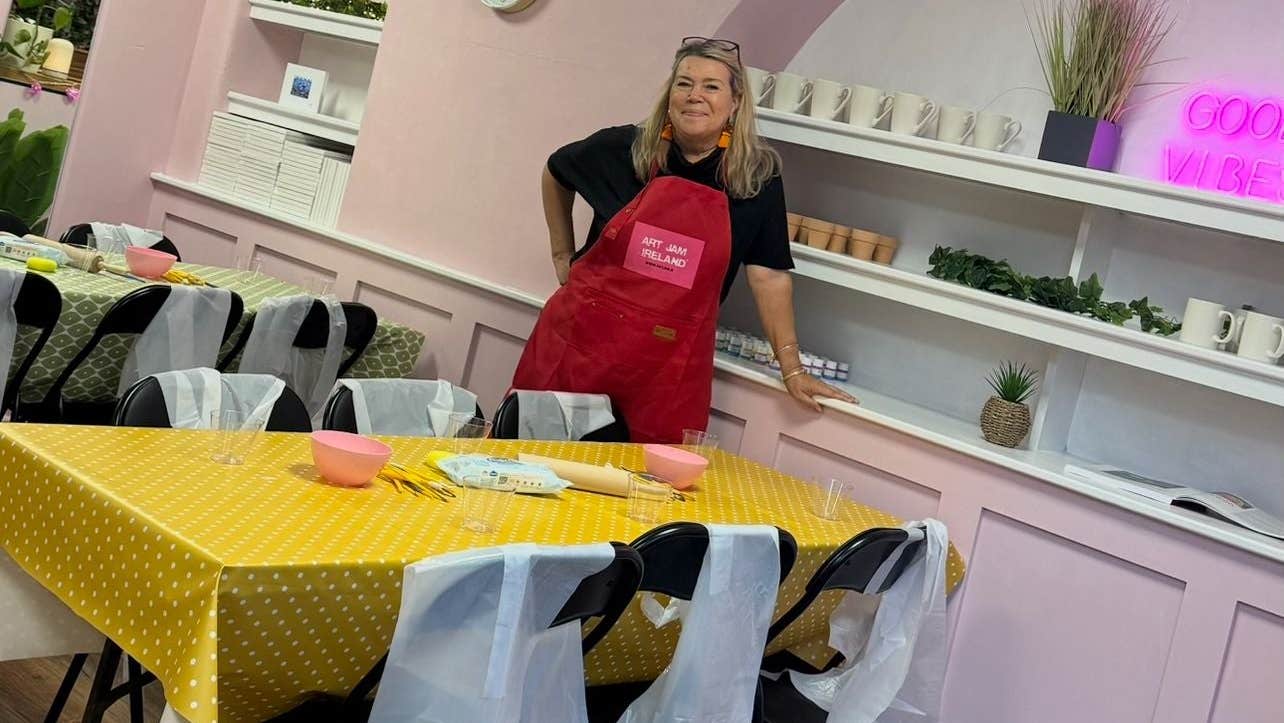 Person wearing a red apron standing by a table with a yellow tablecloth in a room with pink walls