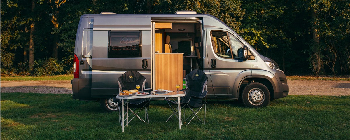 A campervan parked on a grass area with small table and chair beside it