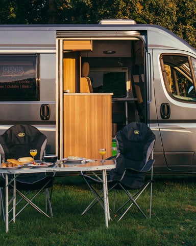 A campervan parked on a grass area with small table and chair beside it