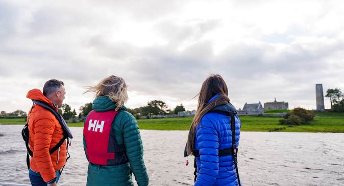 Three people looking out at Clonmacnoise monastic site from a river cruise.