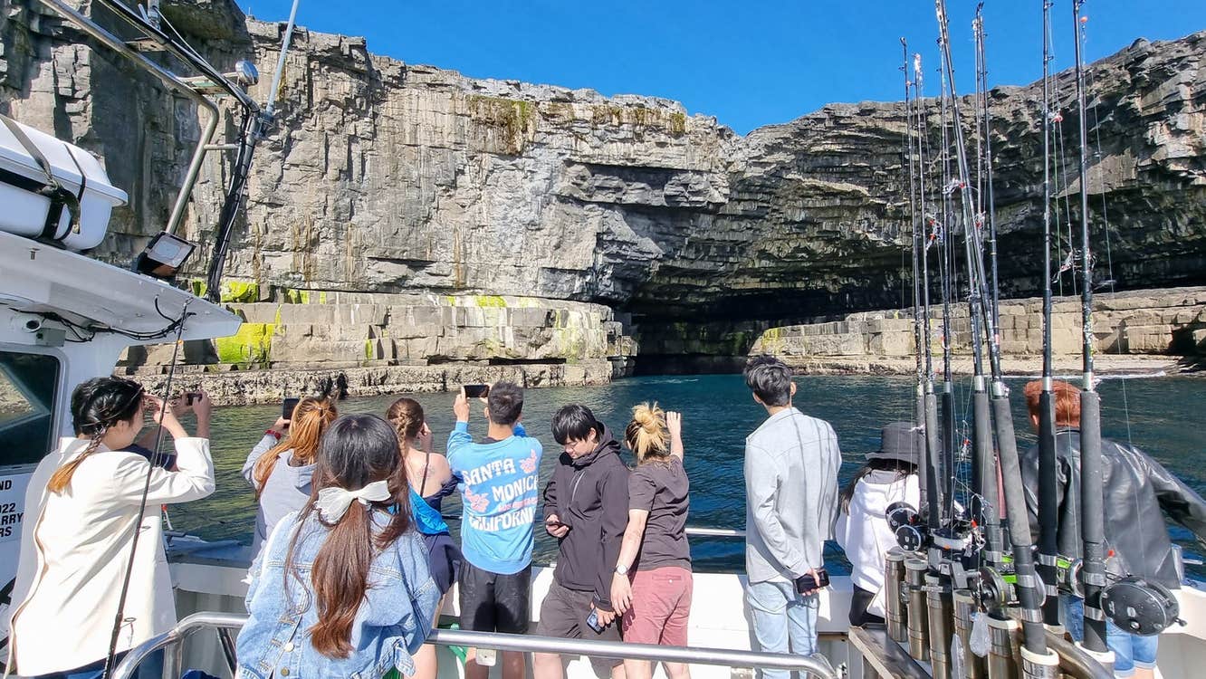A group of people on a boat looking up at a cliff