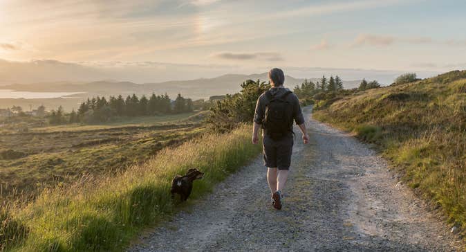 A man and his dog walking in Co. Donegal with views of trees and mountains in the distance