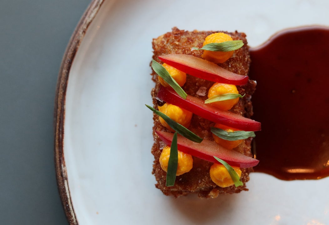 Decorated breaded food with a red sauce on a white plate with a gold rim