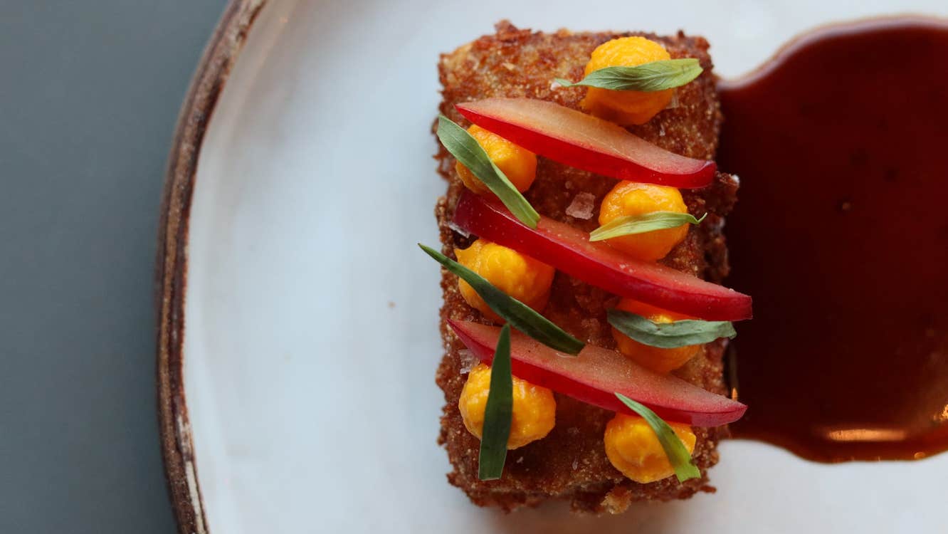 Decorated breaded food with a red sauce on a white plate with a gold rim