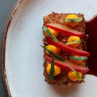 Decorated breaded food with a red sauce on a white plate with a gold rim