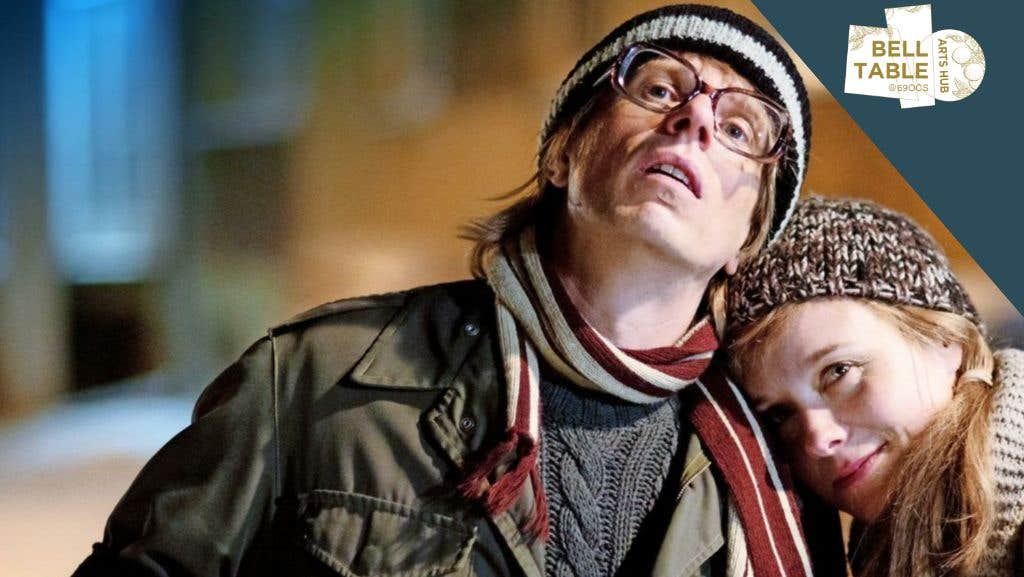 A man in hat and scarf with woman resting her head on his left shoulder.