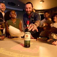 A group of laughing people around a table looking at a bottle of whiskey