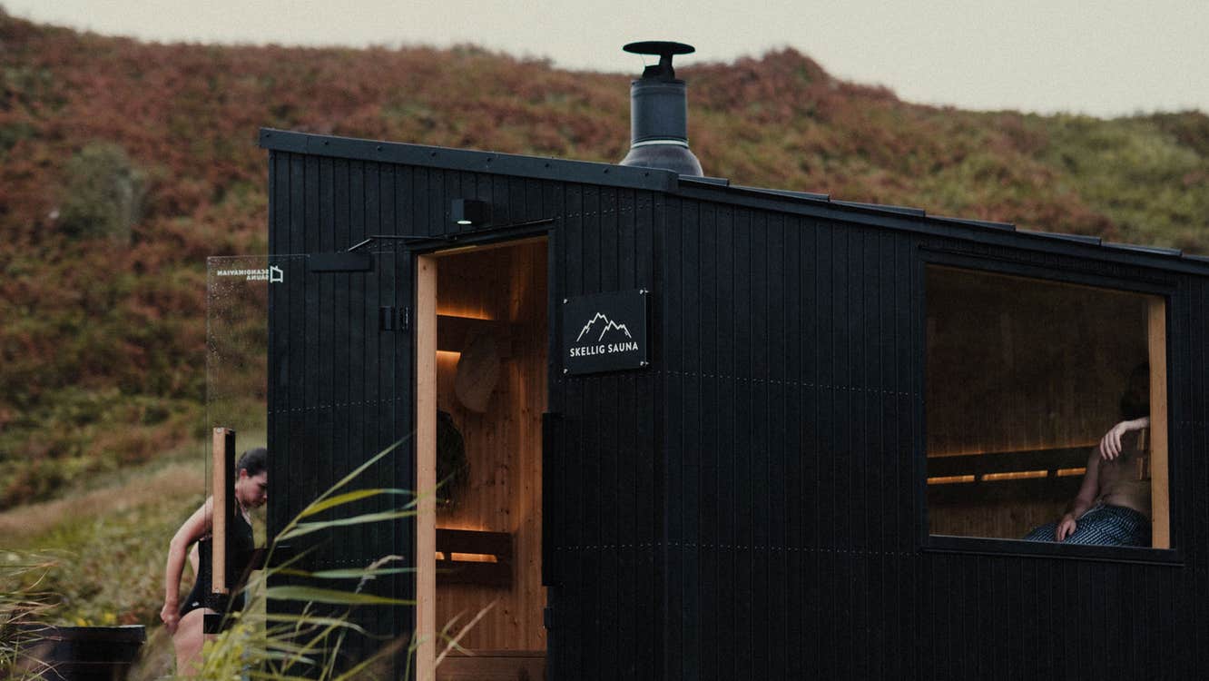 Two people using Skellig Sauna a lady entering the sauna and a gentleman relaxing inside