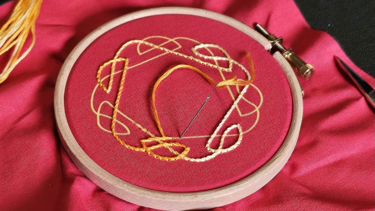 A large piece of red cloth with centre in a round wooden ring with yellow pattern embrioded on.