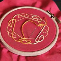 A large piece of red cloth with centre in a round wooden ring with yellow pattern embrioded on.