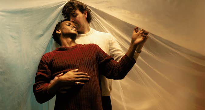 One man is standing behind the other in a gentle embrace