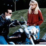 A young woman is speaking to a young man on a motorcycle.