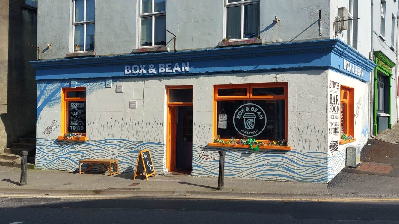 A café with orange window and door frames and a bench and sandwich board outside