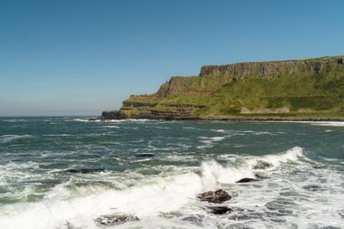 A coastal view with waves crashing on rocks and some cliffs in the distance