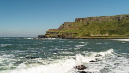 A coastal view with waves crashing on rocks and some cliffs in the distance