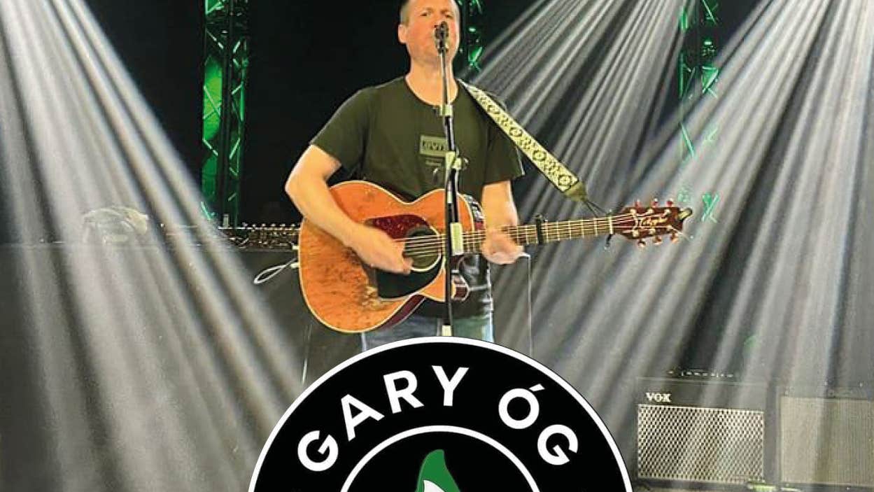 Gary Óg at The Haven, Dunmore East. Photo showing Gary on stage playing guitar and singing with white spot lights and part of logo