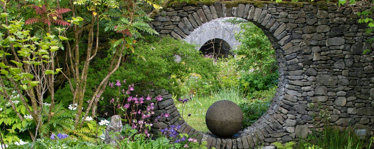 Decorative feature of a large complete circular hole within a stone built wall with the view framed to show an arched bridge in the background
