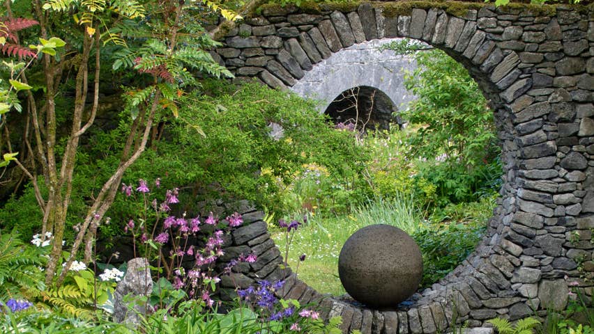 Decorative feature of a large complete circular hole within a stone built wall with the view framed to show an arched bridge in the background