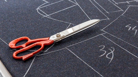 A pair of scissors on the sketched cloth in preparation of cutting the garment designs