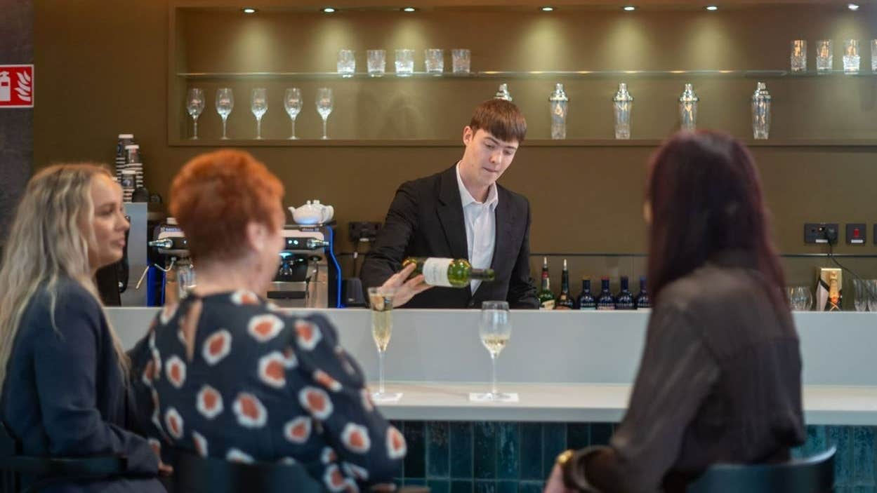 Person serving white wine to three people sitting at the bar