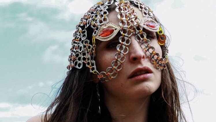 A person with long dark hair wearing a head and partial face covering made from interlinked chains.