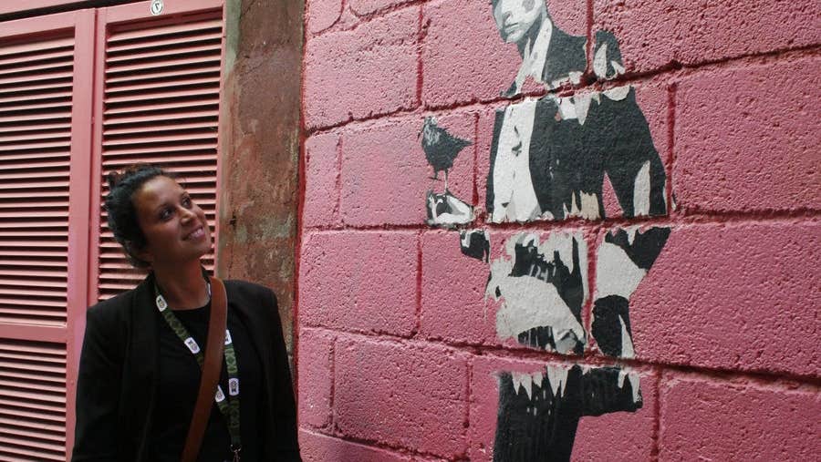 A woman standing by a wall looking up at an image painted on the wall