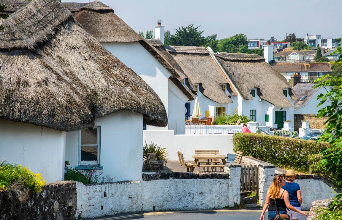 People walking by white thatched cottages in Dunmore East, Co Waterford