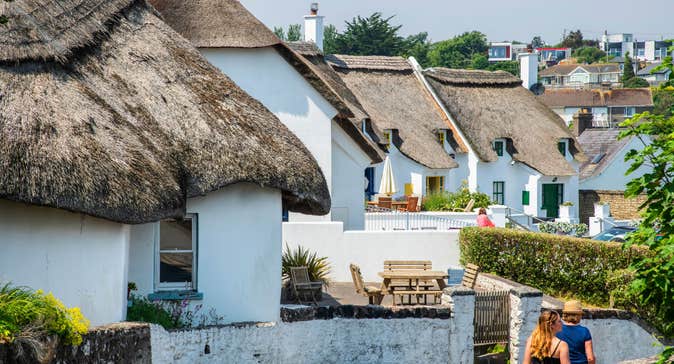 People walking by white thatched cottages in Dunmore East, Co Waterford