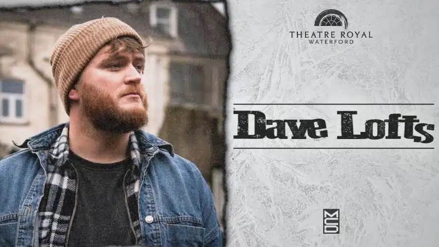 A bearded man in woollen hat and denim jacket outdoors with building behind, looking away to his left.