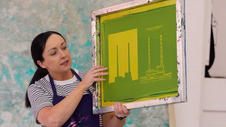 Person wearing a navy apron holding a framed green and yellow print