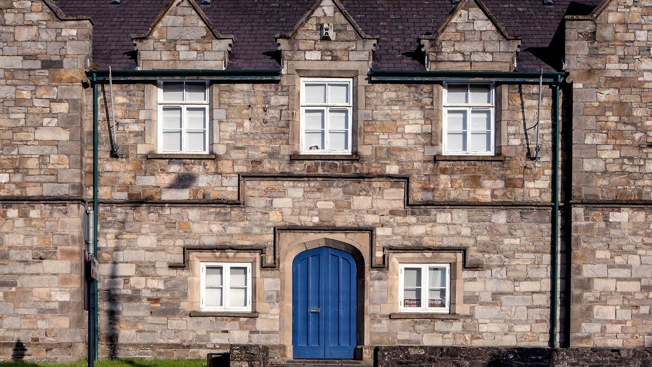 Stone building with five white windows and a blue door and steps in front