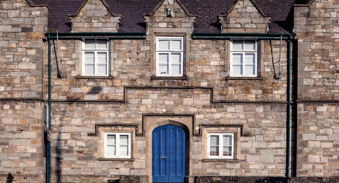 Stone building with five white windows and a blue door and steps in front