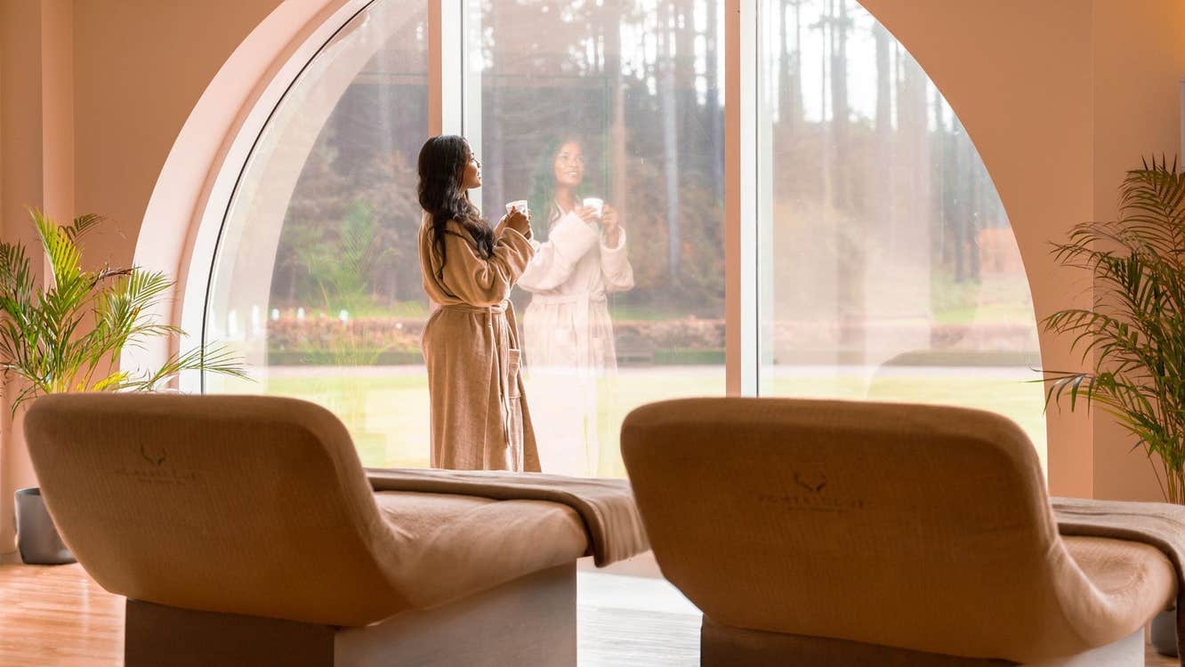 A lady in a bathrobe staring out a large window in a room with treatment beds