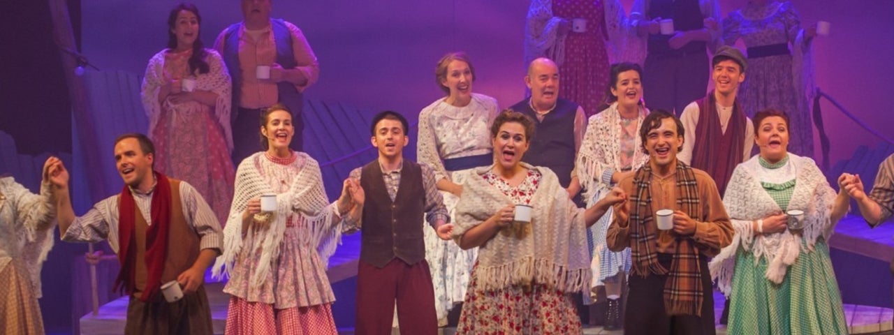 A large group of people in costumes singing on a stage