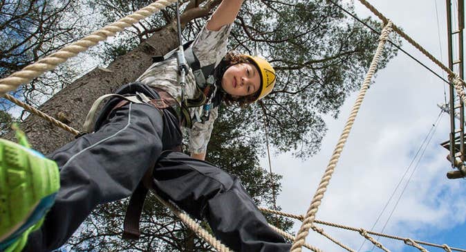 Child looking down at the camera walking on a rope between trees with a blue sky above