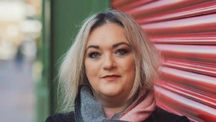 A smiling woman leaning against closed roller blinds over shop window