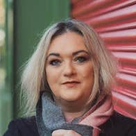 A smiling woman leaning against closed roller blinds over shop window