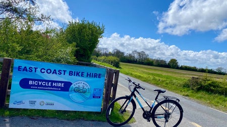 The sign for East Coast Bike Hire and a bike at a road side gateway