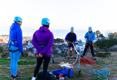 Four people with blue and red ropes standing on top of a rock waiting to abseil