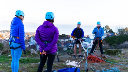 Four people with blue and red ropes standing on top of a rock waiting to abseil