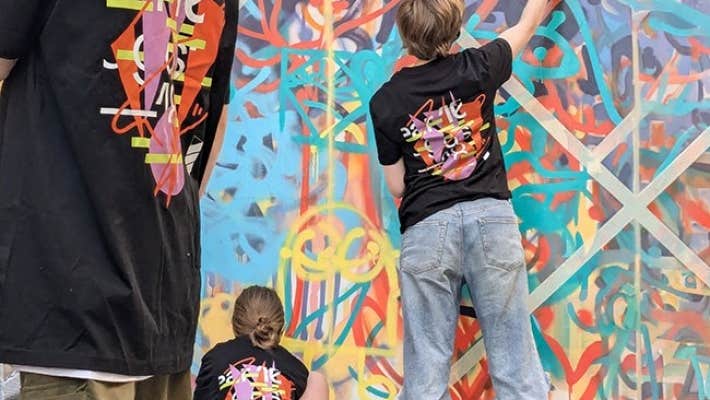Rear view of youngsters in matching T-shirts working on art on a wall