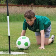 A child on their hands and knees blowing on a football to get it in a hole
